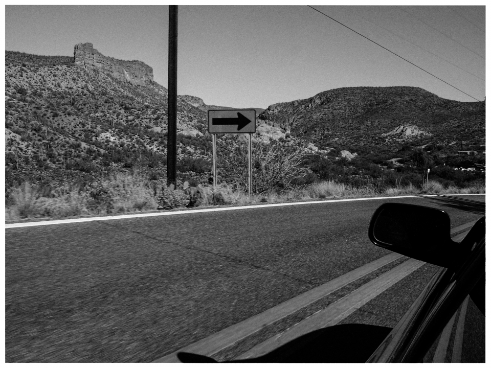 Auto auf Straße in bergiger, trockener Landschaft mit Verkehrsschild nach rechts.