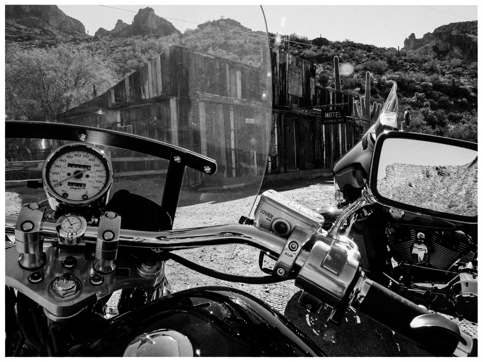 Motorradlenker vor einer alten Westernszene mit Kakteen und Felsen im Hintergrund.