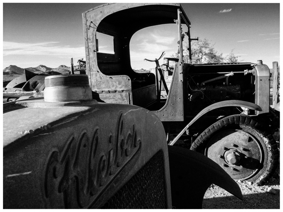 Altes rostiges Fahrzeug mit Kleiber-Logo vor bergiger Kulisse und bewölktem Himmel.