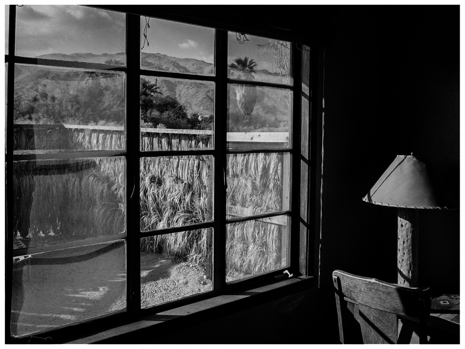 Berglandschaft und Palmen durch Fenster, Lampe und Stuhl im Raum.
