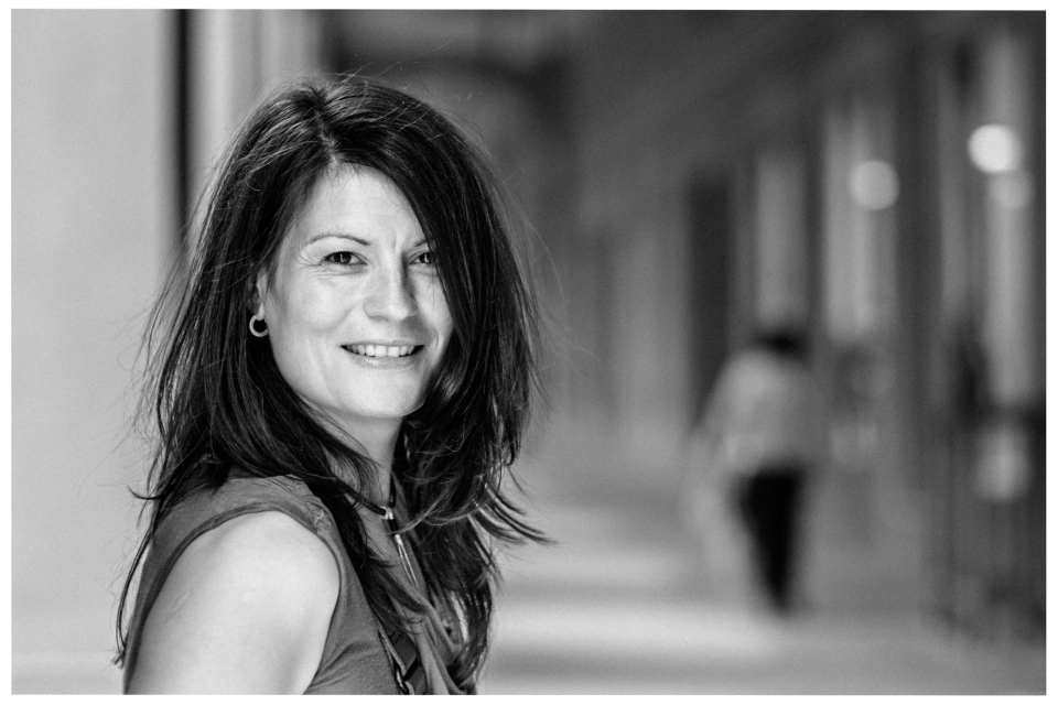 Frau mit schulterlangem Haar lächelt, Schwarz-Weiß, verschwommener Passagierzonen-Hintergrund.