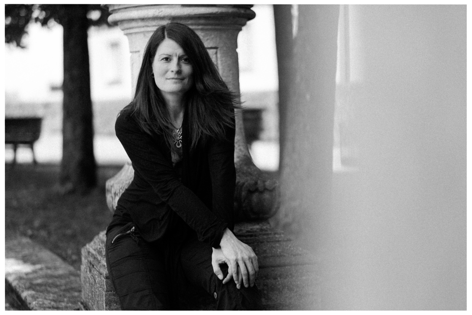 Frau sitzt im Freien auf Steinkonstruktion, Hintergrund unscharfe Bäume, Schwarzweiß-Foto