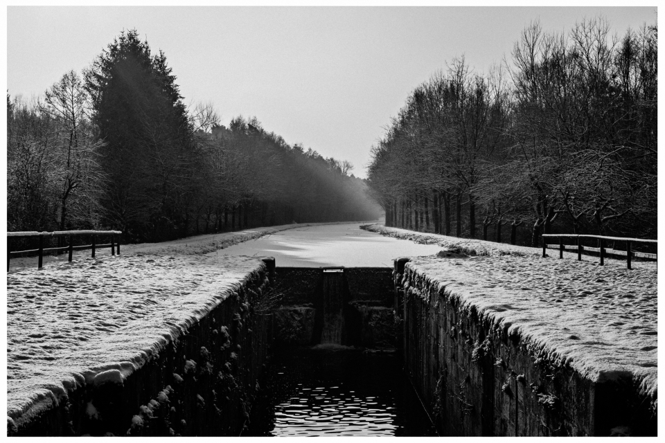 Verschneite Kanallandschaft mit Schleuse, gefrorenem Wasser und schneebedeckten Bäumen.