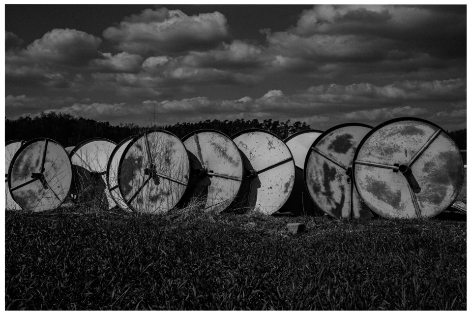 Gruppe großer, rostiger Kabeltrommeln auf grasbewachsenem Feld unter wolkigem Himmel.