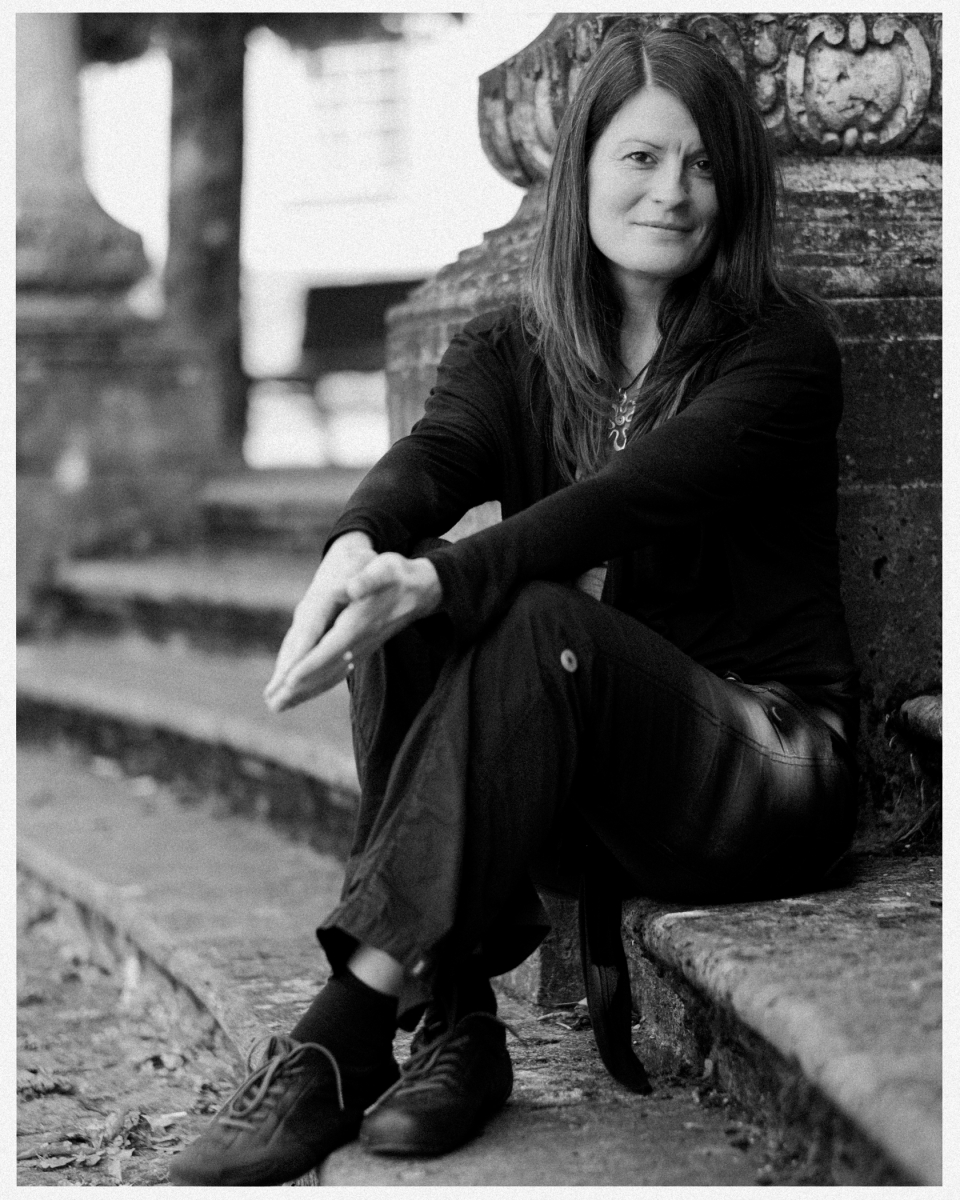 Frau sitzt entspannt lächelnd auf steinerner Treppe neben verziertem Pfeiler, schwarz-weiß.