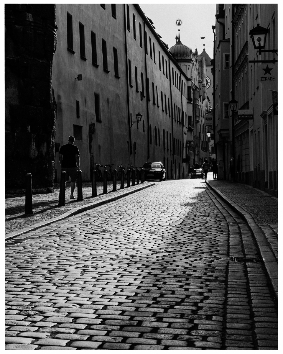 Gepflasterte Straße zwischen hohen Gebäuden mit Türmen, Menschen und Fahrrädern am Straßenrand.
