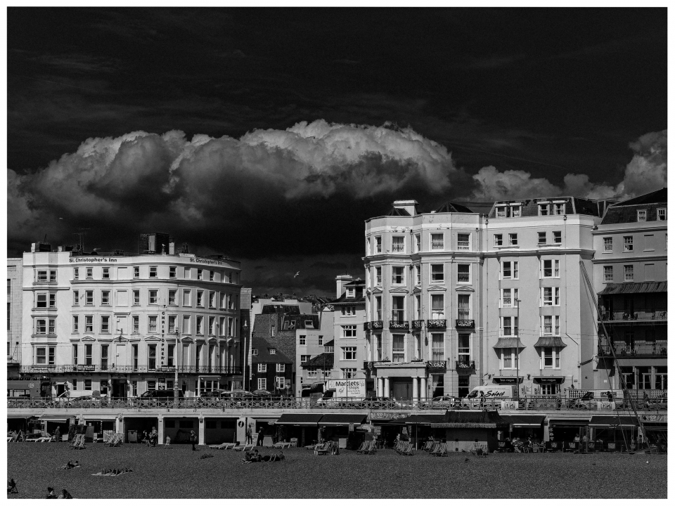 Historische Gebäude am Strand mit dramatischen Wolken und verteilten Liegestühlen.