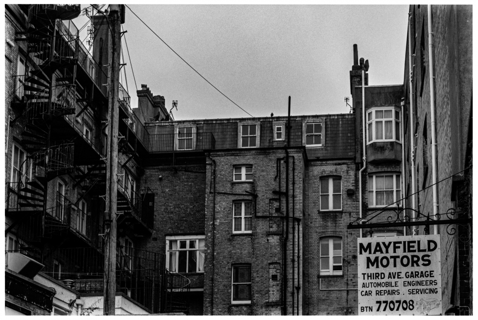 Backsteingebäude mit Feuerleiter und "MAYFIELD MOTORS"-Schild für nahegelegene Garage.