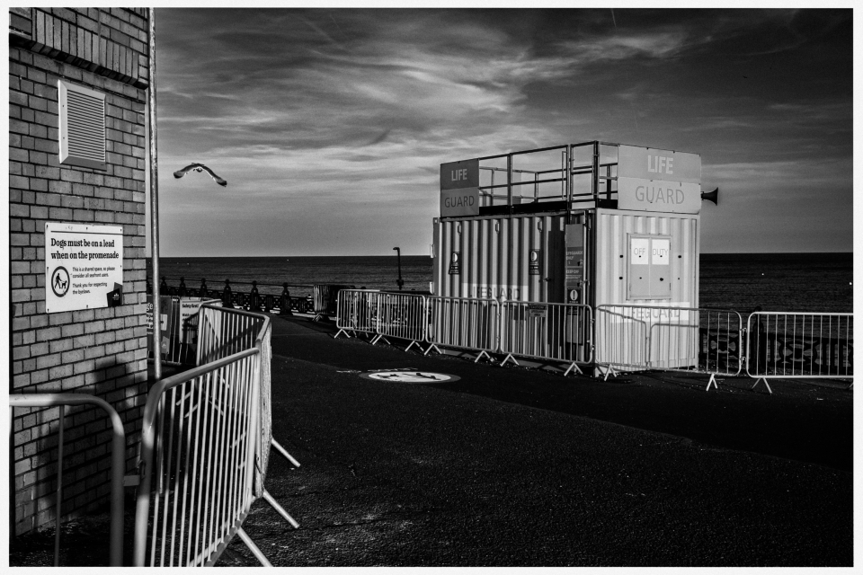 Promenade mit Containermodul-Rettungsturm, Leinenpflicht-Schild, Meer im Hintergrund.
