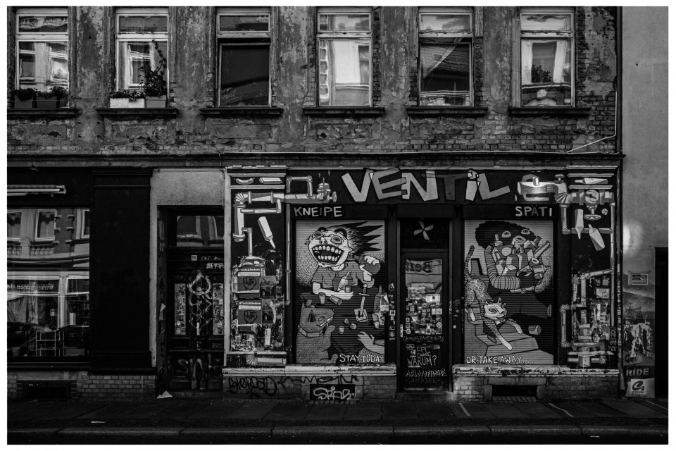 Altes urbanes Gebäude mit bemalten Rollläden, Graffiti, Plakaten; als Kneipe und Späti beschildert.