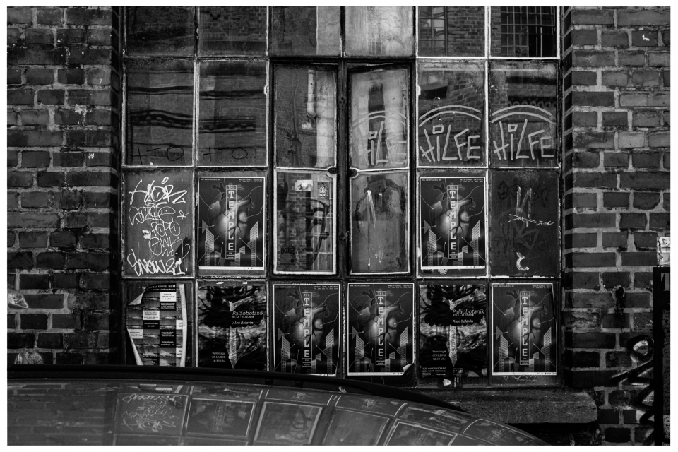 Backsteinmauer mit großen Fenstern, vielen Postern, Graffiti und Spiegelung von Gebäuden.