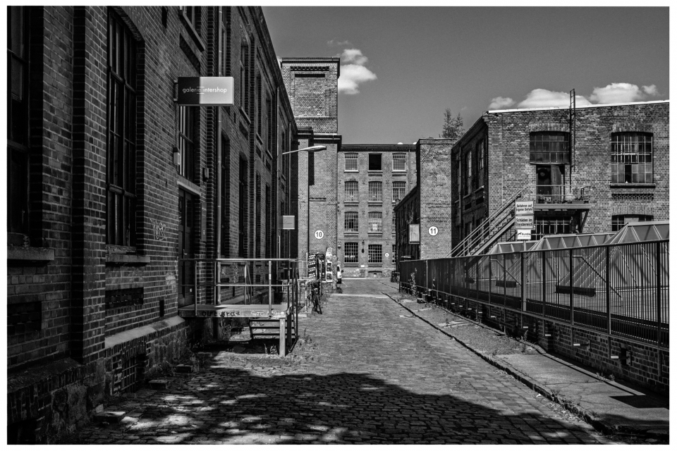 Gepflasterter Innenhof historischer Backsteinfabrik, umgeben von mehrstöckigen Gebäuden.