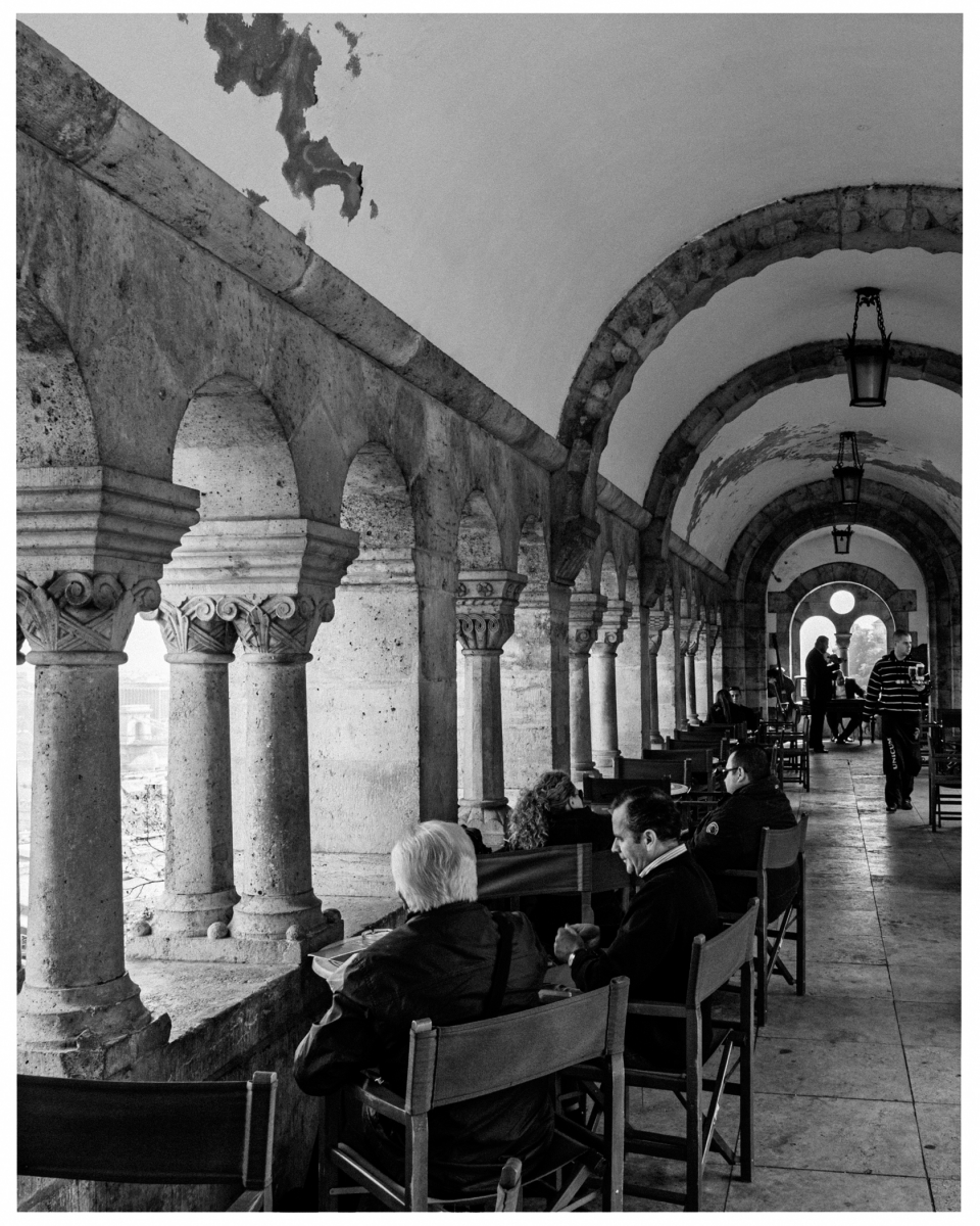 Historische Arkade mit Rundbögen, Personen sitzen und genießen die Aussicht durch die Säulen.