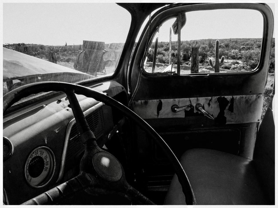 Innenraum eines alten Autos mit kaputtem Dashboard, Wüste und Kakteen durch Fenster sichtbar.