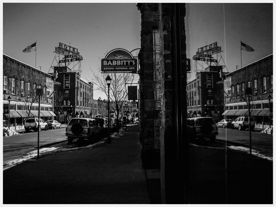 Schwarz-weiße Straßenszene mit geparkten Autos, Geschäft "Babbitt's" und Gebäuden im Hintergrund.