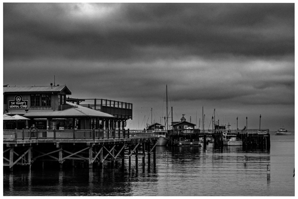 Pier mit Geschäft und Booten im Hafen an einem bewölkten Tag, Schwarz-Weiß-Foto.