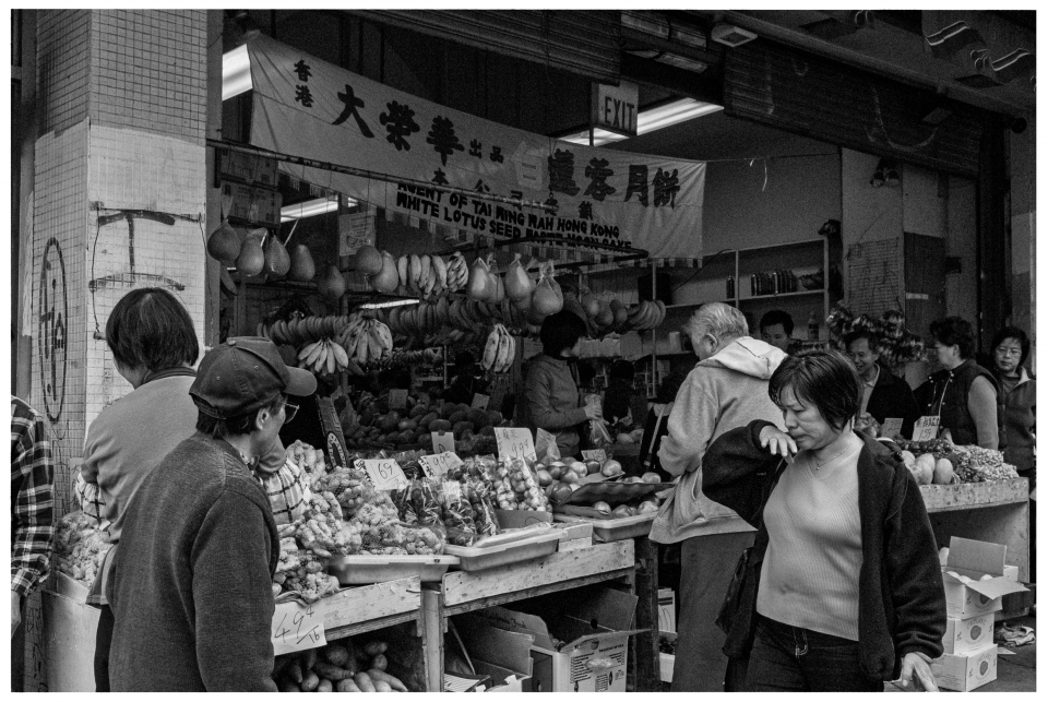 Asiatischer Markt, viele Menschen, Obst- und Gemüsestände, Schilder auf Chinesisch und Englisch.