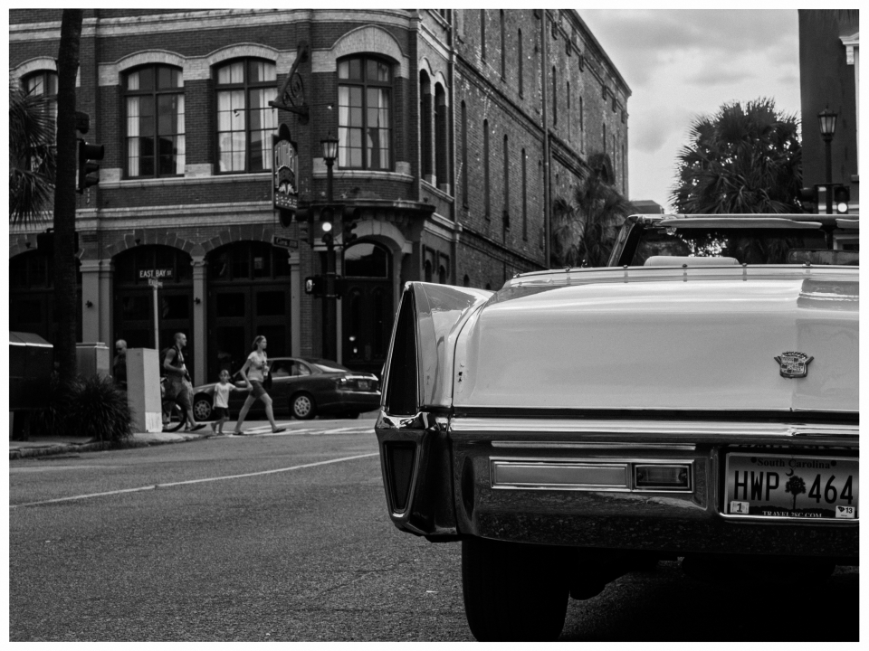 Klassisches Auto mit South Carolina-Nummernschild vor Ziegelgebäude und Palmen auf Stadtstraße.