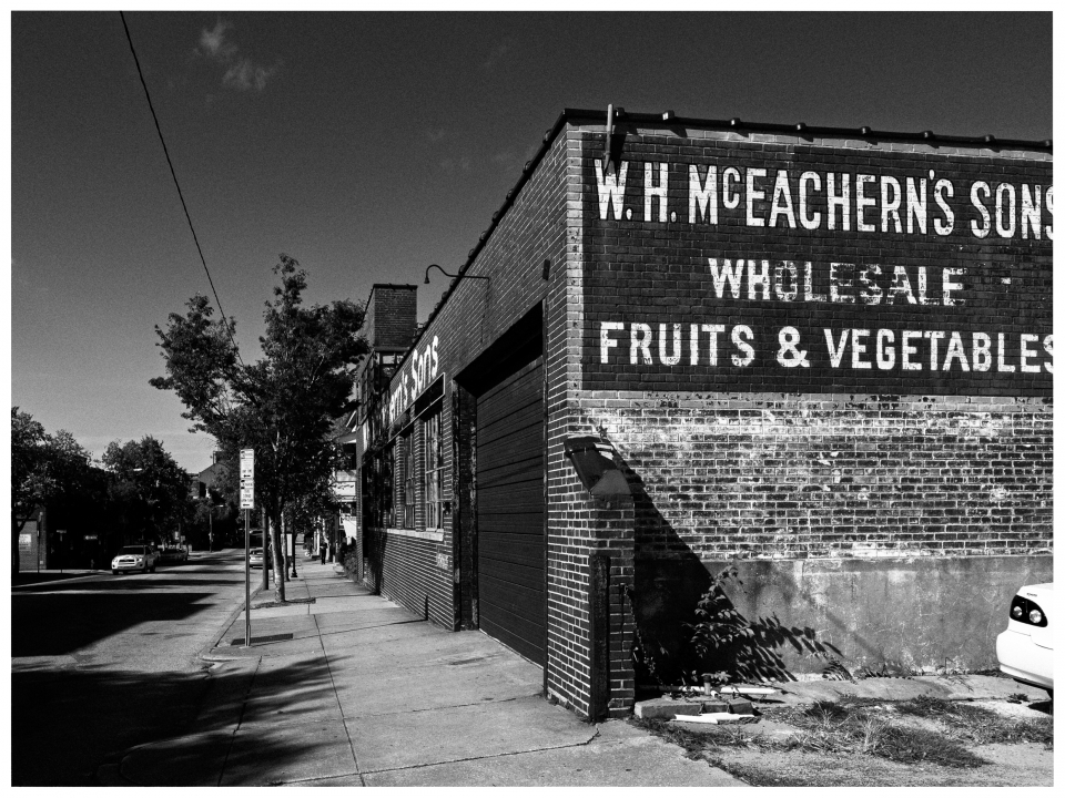 Ein schwarzes Auto parkt vor einem Backsteingebäude mit „W.H. McEachern's Sons“ am Gehweg.