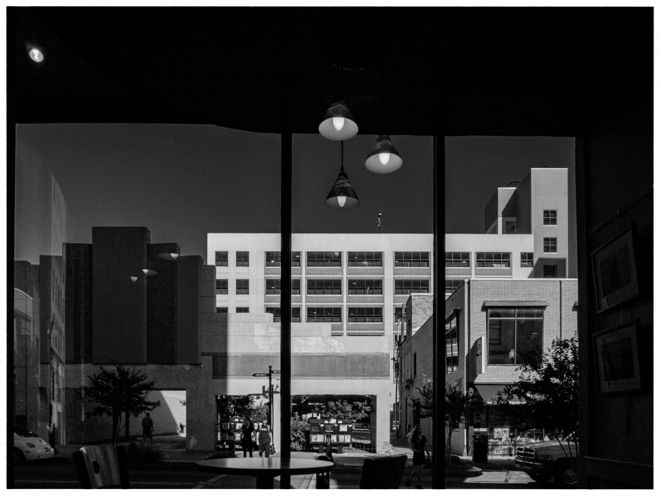 Café-Ansicht durch Glasfront, zeigt Straße mit modernen Gebäuden, Menschen und Fahrzeugen.