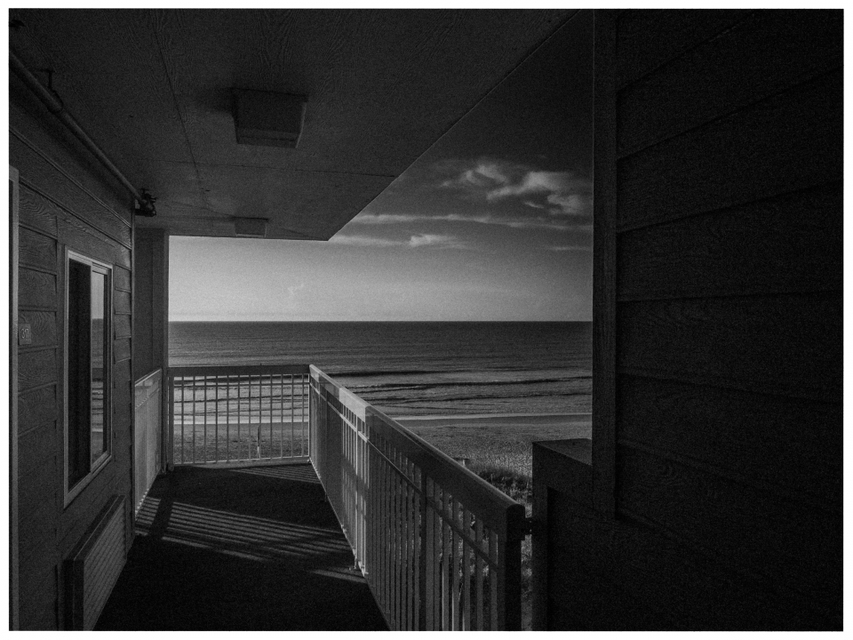 Balkon mit Meerblick, Gebäudewänden, bewölkter Himmel und Wellen, Schwarz-Weiß-Foto.