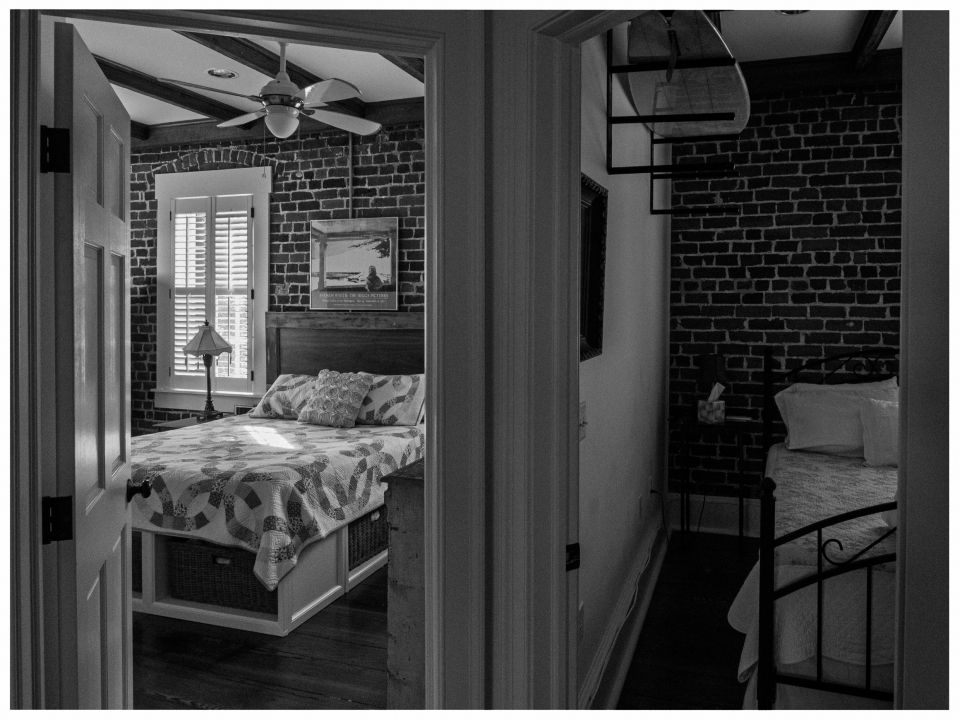 Zwei angrenzende Schlafzimmer mit Backsteinwänden, Holzbalkendecken und gemusterten Betten.