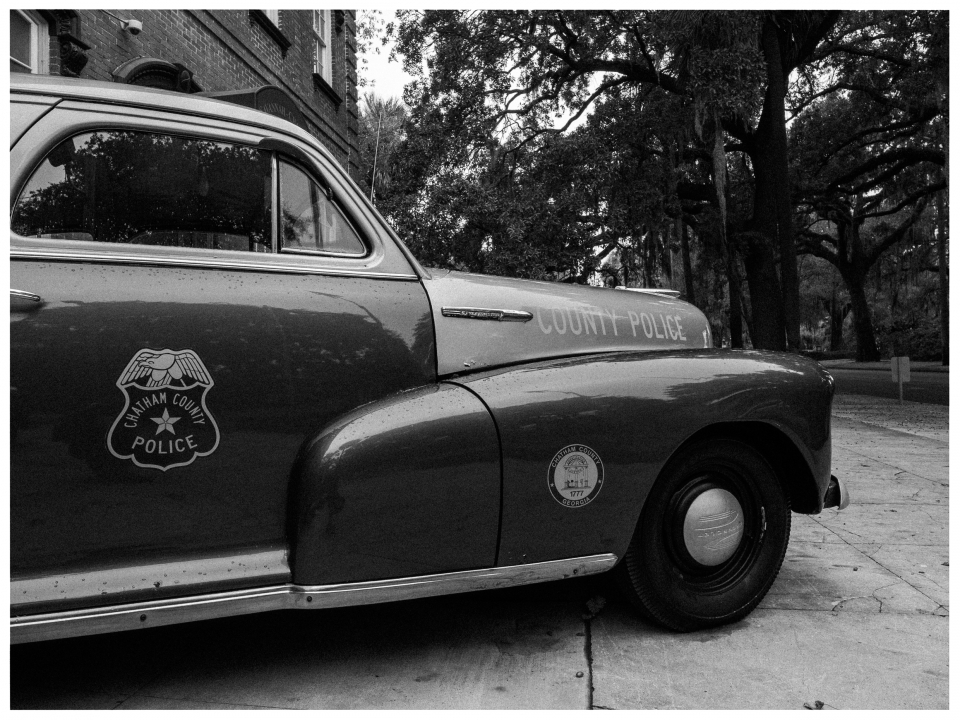 Old Chatham County Police car by roadside, black-and-white, with trees in background.
