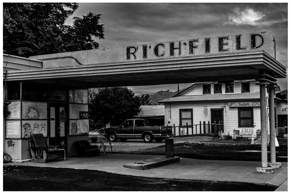Old gas station with "RICHFIELD" sign, chairs and black pickup in front of a white building.