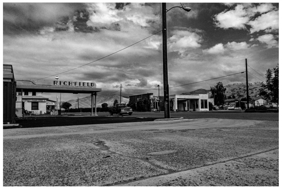 Verlassene Richfield-Tankstelle in schwarz-weißer Szenerie mit Pickup und Gebäuden.