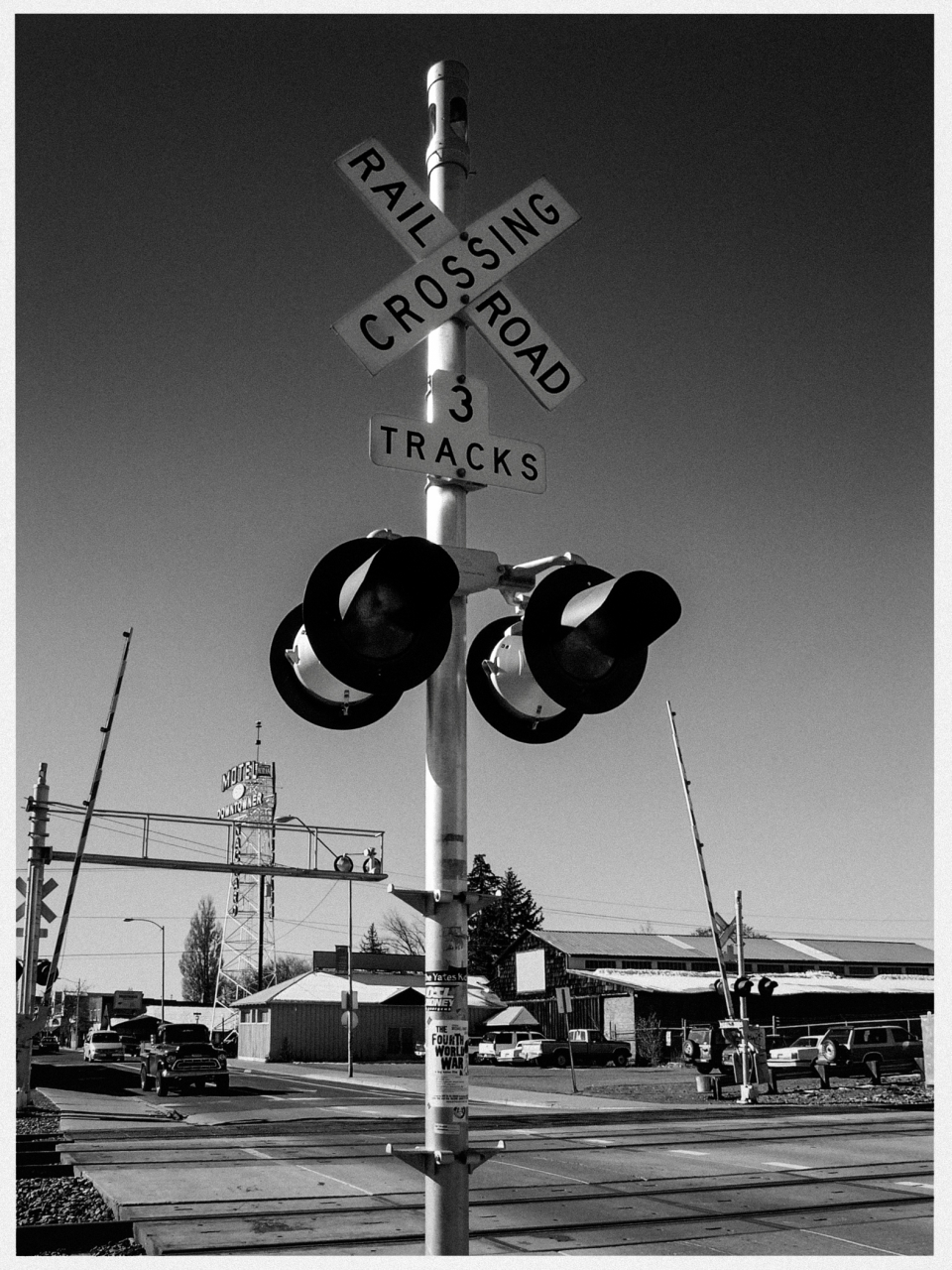 Bahnübergang mit drei Gleisen, Kreuzungsschild, Signalleuchten, Autos, Gebäude, Motel-Schild.