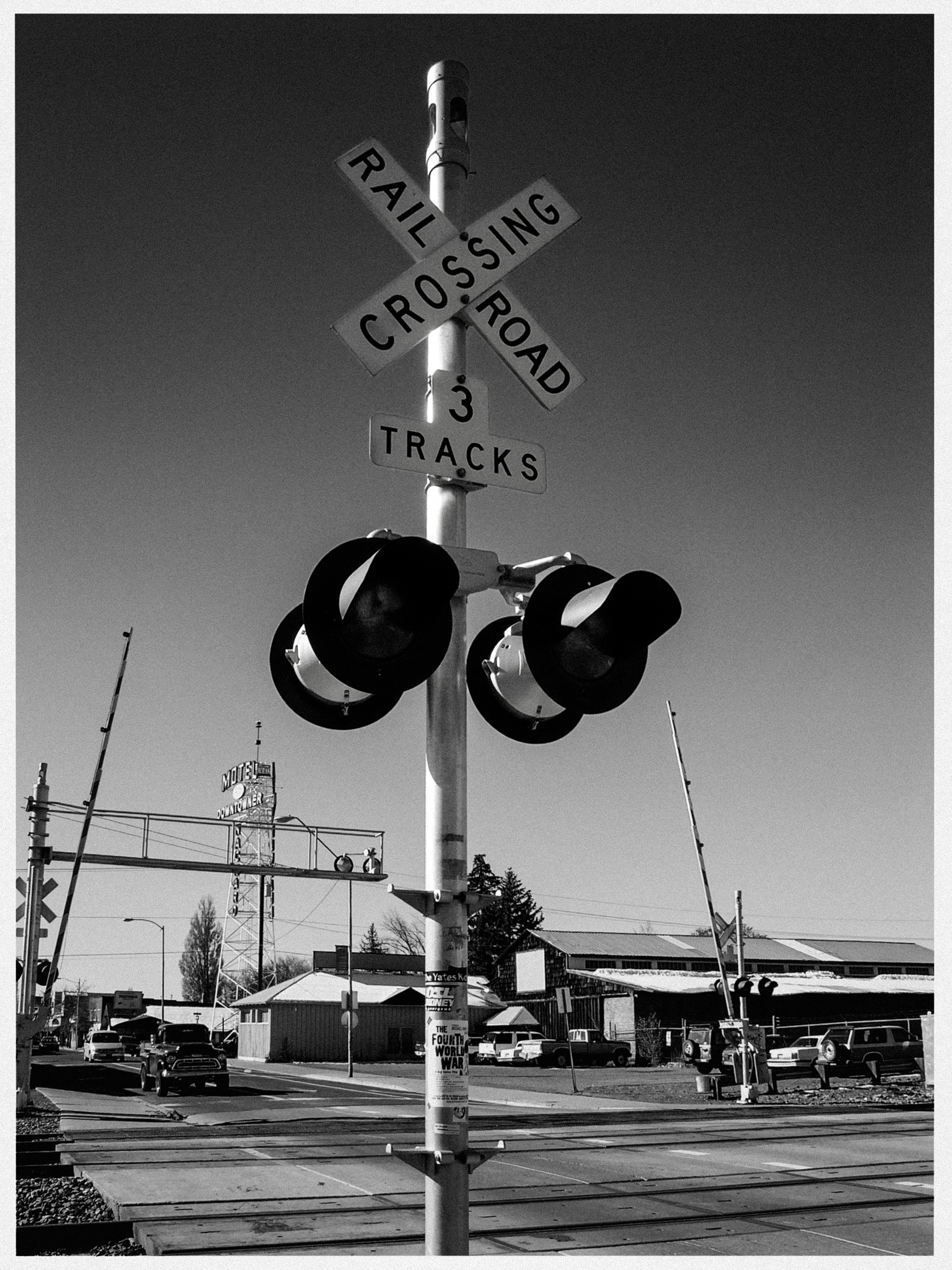 Bahnübergang mit drei Gleisen, Kreuzungsschild, Signalleuchten, Autos, Gebäude, Motel-Schild.