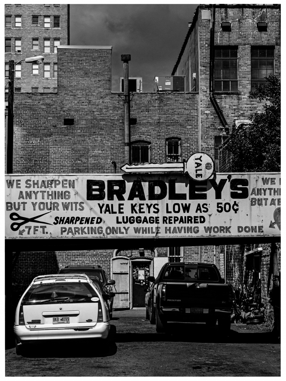 Städtische Szene mit engem Durchgang, Schild für Dienstleistungen, zwei parkende Fahrzeuge vorne.