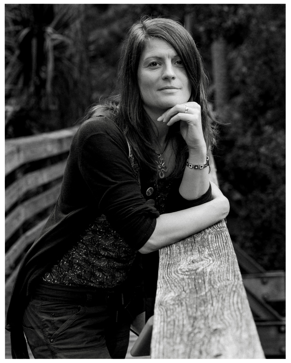 Frau lehnt nachdenklich an hölzerner Brüstung im Freien, Schwarz-Weiß-Aufnahme.