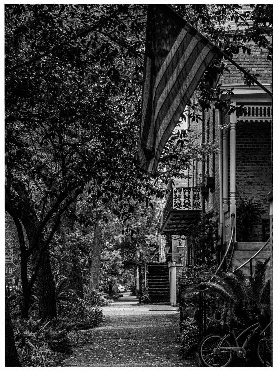 Ein Gehweg mit Bäumen, Backsteinhaus, Treppe, Balkon, US-Flagge und Fahrrad im Vordergrund.