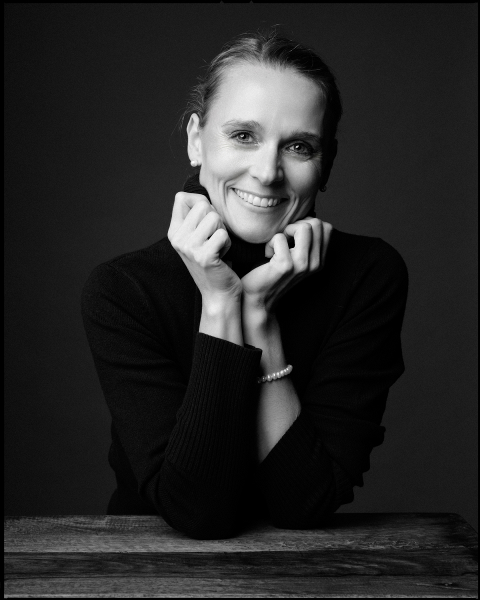 Schwarz-weiß Porträt einer Person mit Rollkragenpullover, Kopf auf Händen, lächelnd, dunkler Hintergrund.