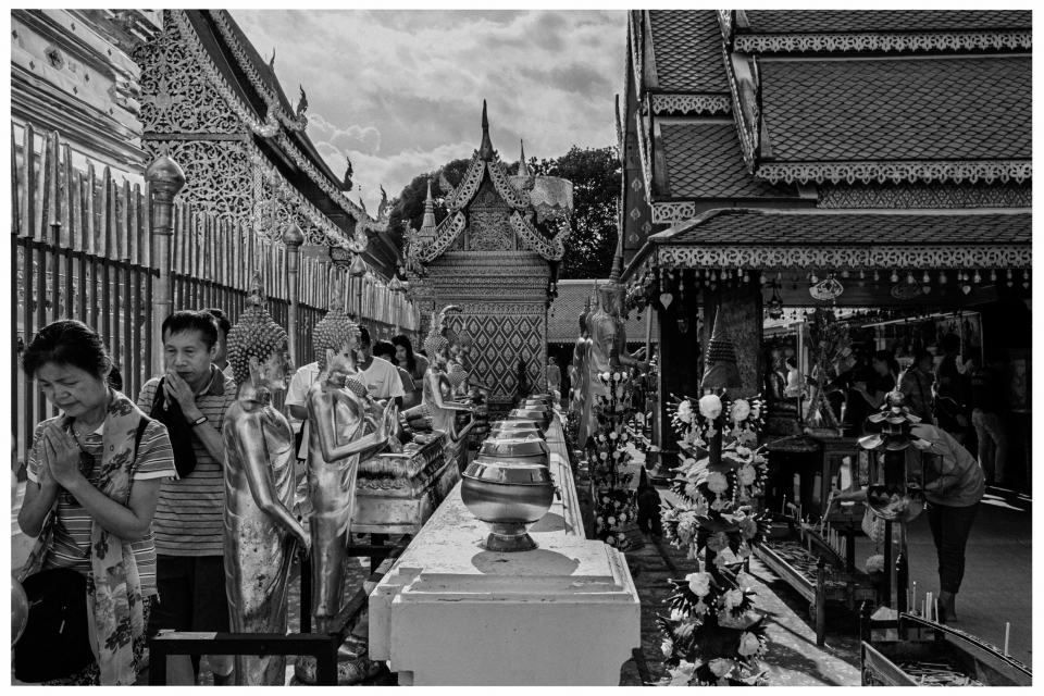 Traditioneller thailändischer Tempel mit reich verzierten Dächern und betenden Menschen.