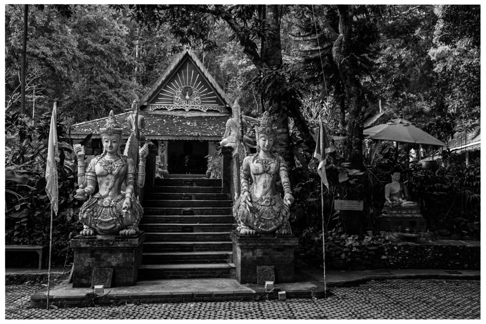Tempelportal mit Statuen, Treppe und dekorativem Dach, umgeben von üppiger Vegetation.