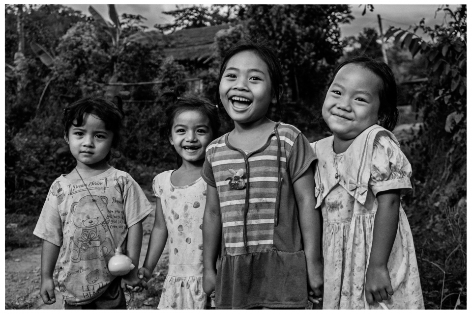 Vier Kinder stehen lächelnd im Freien, umgeben von Pflanzen und Bäumen.