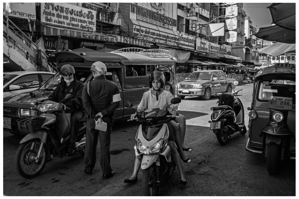 Städtische Szene mit Motorrädern, Verkehrspolizist, Autos, Tuk-Tuk und Straßenschildern.