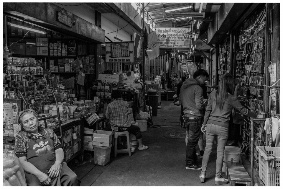 Personen stöbern in überdachtem Markt mit Verkaufsständen und Waren.