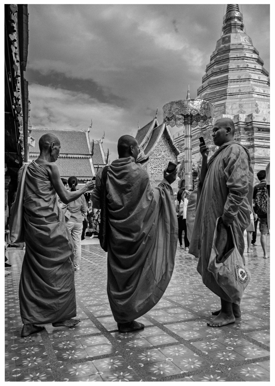 Mönche mit Mobiltelefonen auf dekorativem Platz vor Tempel mit goldfarbenem Dach.