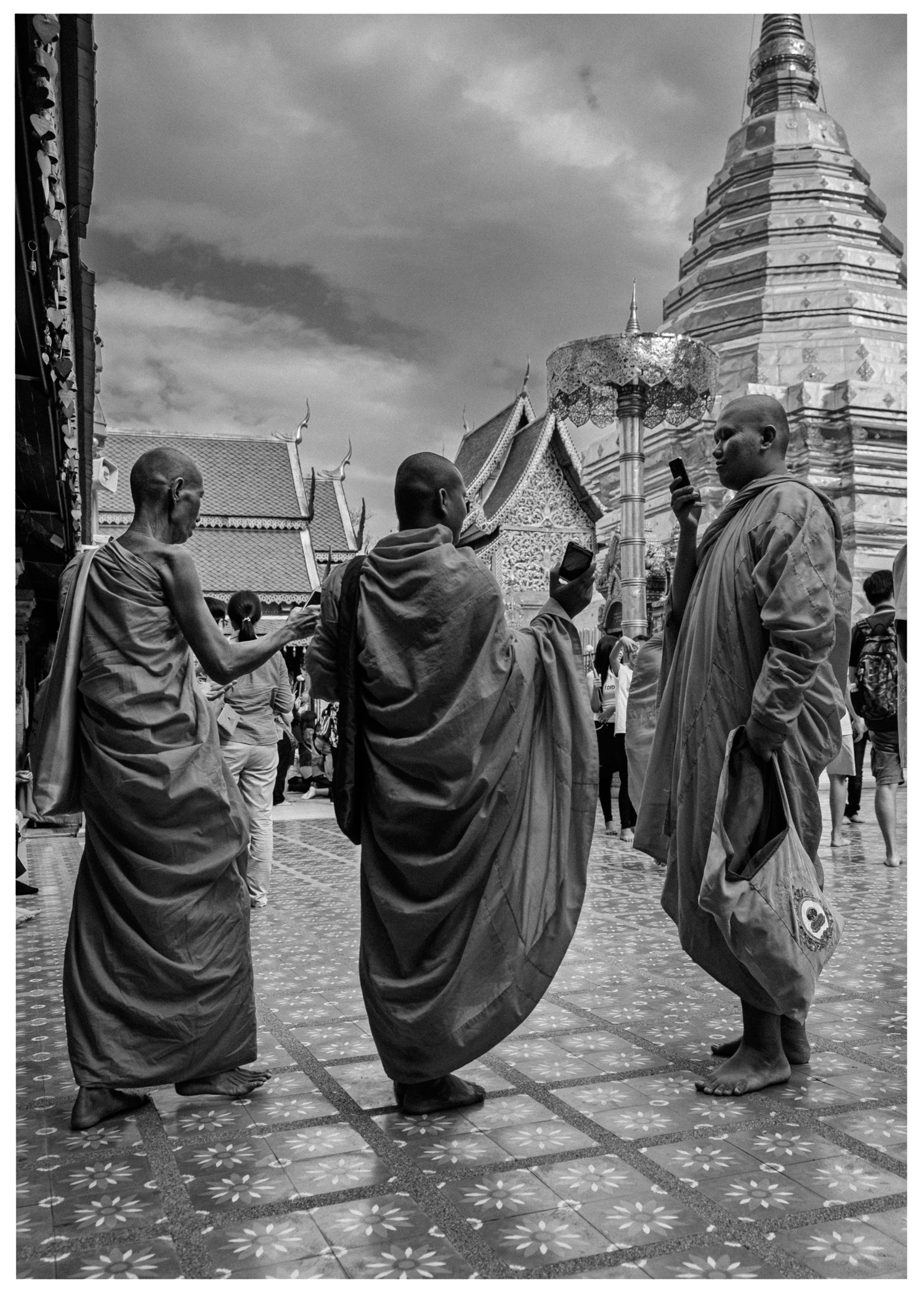 Mönche mit Mobiltelefonen auf dekorativem Platz vor Tempel mit goldfarbenem Dach.