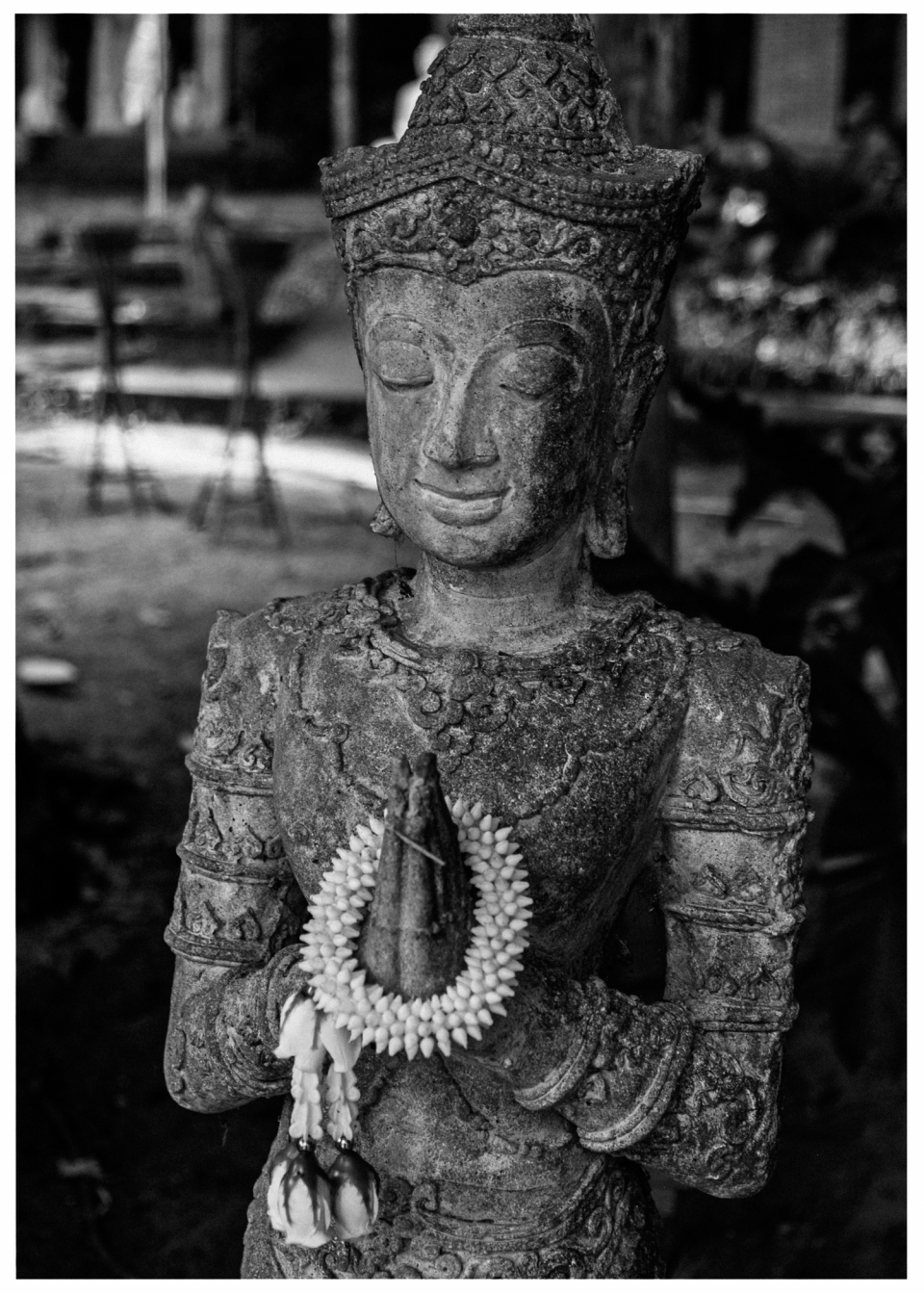 Steinerne Statue einer Figur mit Blumenkranz, geschlossenen Augen und gefalteten Händen