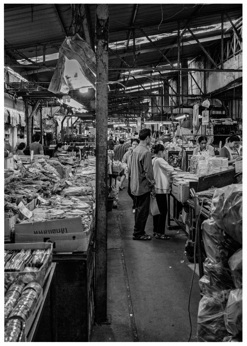 Überdachter Markt mit Ständen, Menschen betrachten Produkte, geschäftige und dichte Atmosphäre.