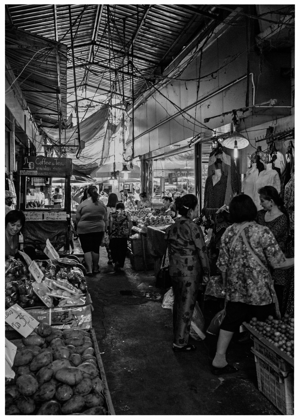 Belebter überdachter Marktgang mit Menschen, Ständen für Obst, Gemüse und Kleidung.