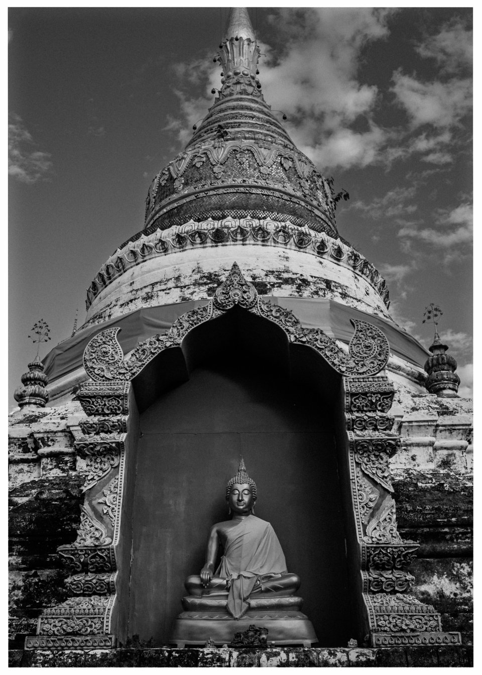 Pagode mit Buddha-Statue und Ornamenten vor bewölktem Himmel.